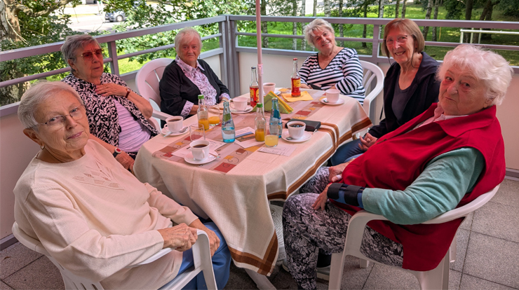sechs Frauen sitzen gut gelaunt an einem Tisch auf der Terrasse